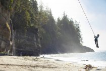 Young woman swinging on rope at Mystic Beach along Juan de Fuca Trail, Vancouver Island, Canada — Stock Photo