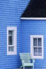Exterior de casa azul con ventanas blancas y silla de madera verde - foto de stock