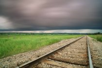 Railroad tracks with storm clouds over meadow near Didsbury, Alberta, Canada — Stock Photo