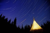 Star trails over illuminated tee-pee by Canim Lake band in Cariboo Mountains, British Columbia, Canadá . — Fotografia de Stock