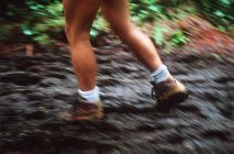 Piernas femeninas senderismo por sendero fangoso en el bosque - foto de stock