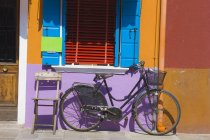 Vieja bicicleta y silla apoyada en la pared pintada de colores, isla de Burano, Venecia, Italia - foto de stock