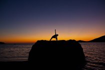 Silhouette de femme pratiquant le yoga sur le rocher côtier au lever du soleil à Kalymnos, Grèce
. — Photo de stock