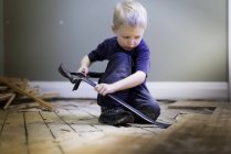 Vorschulkind spielt Tischler mit Brechstange, Hammer und Hartholzboden. — Stockfoto