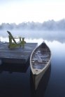 Canoa de madeira amarrada no cais com cadeira de pátio no lago Muskoka em Ontário, Canadá — Fotografia de Stock