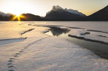 Salida del sol junto al Monte Rundle reflexionando sobre el hielo en el lago Vermilion cubierto de nieve en invierno en el Parque Nacional Banff, Alberta, Canadá . - foto de stock