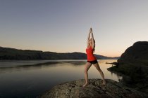 Mujer joven practicando arte de yoga sobre el lago Kamloops al atardecer, Kamloops, Columbia Británica, Canadá - foto de stock