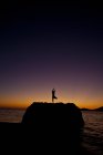 Silhouette of woman practicing yoga on coastal rock at sunrise in Kalymnos, Greece. — Stock Photo