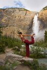 Young woman practicing yoga beneath Takakkaw Falls in Yoho National Park, British Columbia, Canada — Stock Photo