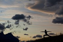 Silhueta de mulher praticando ioga na colina ao nascer do sol em Canmore, Alberta, Canadá — Fotografia de Stock