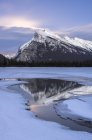 Moonrise behind clouds over Mount Rundle reflecting in Vermilion lake in winter in Banff National Park, Alberta, Canada. — Stock Photo