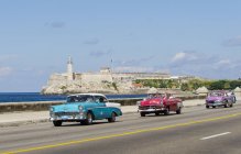 Carros americanos vintage montados ao longo de Malecon com vista pitoresca da fortaleza do Castelo Morro, baía de Havana, Havana, Cuba — Fotografia de Stock