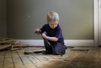 Preschooler boy playing carpenter with crowbar, hammer and hardwood floor. — Stock Photo