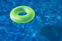Зелена іграшка з плаваючою кільцем у блакитній воді басейну — стокове фото