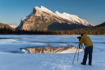 Photographer composing a photograph of Rundle Mount on frozen Vermilion Lakes in winter in Banff National Park, Alberta, Canada. — Stock Photo