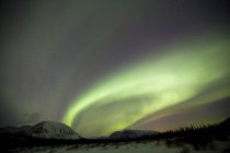 Northern lights with stars above mountains outside of Whitehorse, Yukon, Canada. — Stock Photo