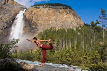 Jovem praticando ioga sob Takakkaw Falls no Parque Nacional Yoho, Colúmbia Britânica, Canadá — Fotografia de Stock