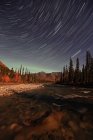 Senderos de estrellas sobre el río Wheaton con Aurora vista en la distancia, Yukón, Canadá . - foto de stock
