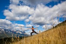 Fit woman practicing yoga warrior posture on hill in backcountry of Canmore, Canada — Stock Photo