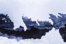 Montagnes rocheuses formant un cadre de glace et de neige sur l'eau dans le ruisseau, Colombie-Britannique, Canada . — Photo de stock
