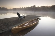 Moored wooden canoe at pier with patio chair on Muskoka lake in Ontario, Canada — Stock Photo