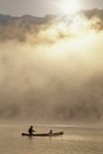 Silhouettes d'hommes et d'enfants en canot par un matin d'été brumeux, lac Alta à Whistler, Colombie-Britannique, Canada — Photo de stock