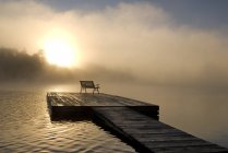Misty sunrise from dock with bench on Oxtongue Lake, Ontario, Canada — Stock Photo