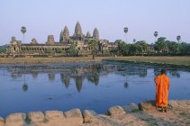 Monje budista de pie frente a un estanque reflectante del templo Angkor Wat, Siem Reap, Camboya - foto de stock
