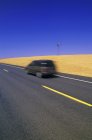 Auto bewegt sich auf breiter Fahrbahn in goldenem Feld in Palouse, Washington State, USA — Stockfoto