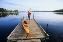 Rear view of male kayaker with kayak on boat dock, Nutimik Lake campground, Whiteshell Provincial Park, Manitoba, Canada. — Stock Photo