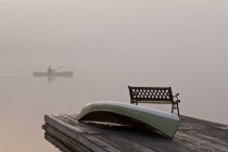 Muelle con banco y barco y silueta de hombre remando canoa en Oxtongue Lake, Muskoka, Ontario . - foto de stock