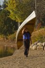 Uomo maturo che trasporta canoa dall'acqua, Oxtongue Lake, Muskoka, Ontario, Canada . — Foto stock
