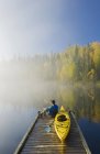 Uomo seduto al molo con kayak, lago Dickens, Saskatchewan settentrionale, Canada — Foto stock