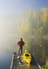 Uomo in piedi con le mani sui fianchi sul molo con kayak, lago Dickens, Saskatchewan settentrionale, Canada — Foto stock