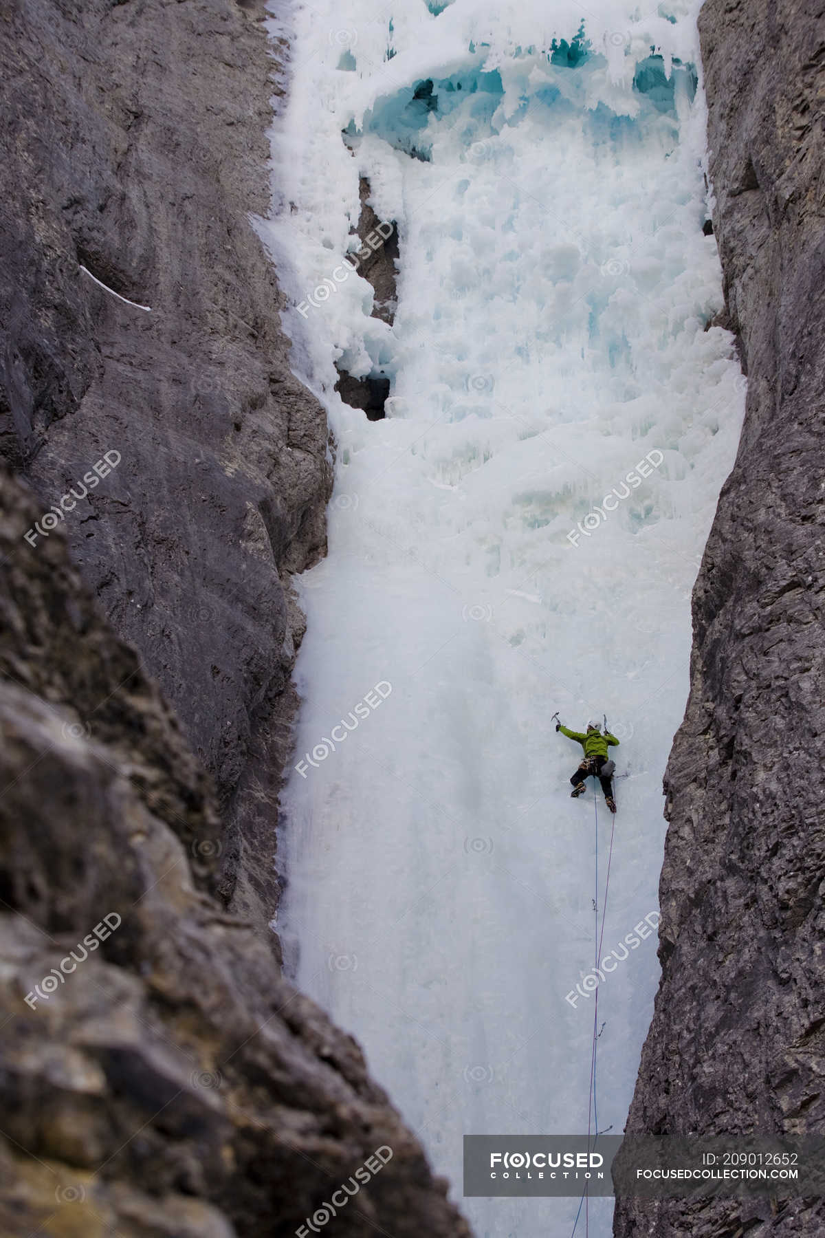 Male ice climber swinging axes into rock face of mountains of Ghost River, Alberta, Canada