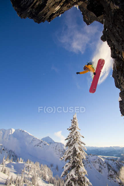 Мужчина-сноубордист прыгает со скалы на сплитборде в Revelstoke Mountain Resort, Revelstoke, Канада — стоковое фото