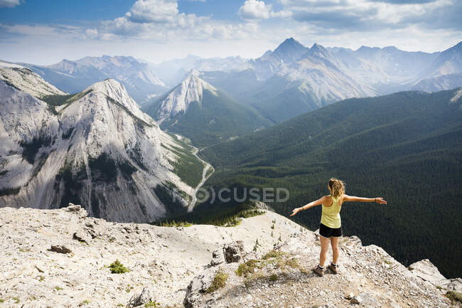 A young woman stands at the summit of the Sulphur Skyline Trail with a view of the Rocky Mountains. Miette Hotsprings, Jasper National Park, Alberta, Canada. — Stock Photo