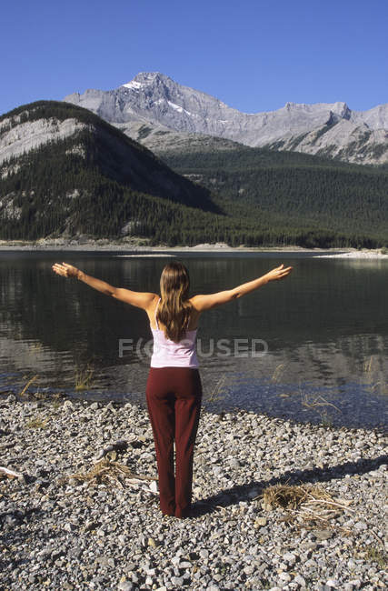 Mujer practicando yoga a lo largo de la orilla de Spray Lakes, Kananaskis Country, Alberta, Canadá . - foto de stock