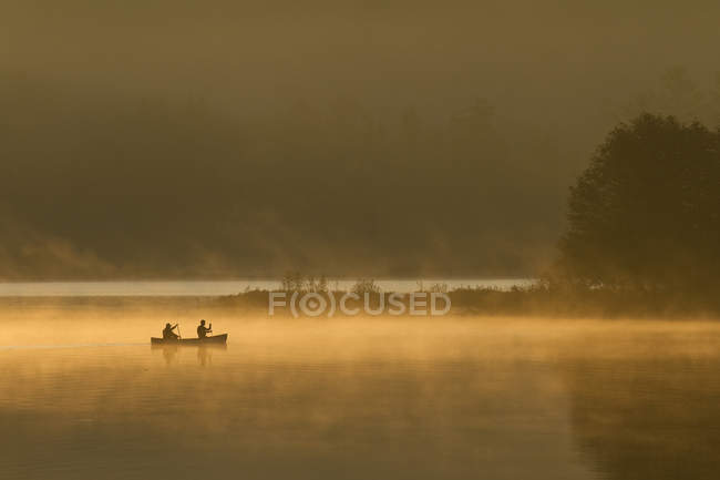 Due uomini che remano in canoa all'alba sul lago Oxtongue, Muskoka, Ontario, Canada . — Foto stock