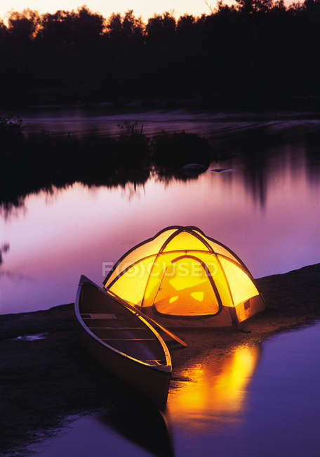 Silueta de pareja acampando en tienda a orillas del río, Whiteshell River, Whiteshell Provincial Park, Manitoba, Canadá - foto de stock
