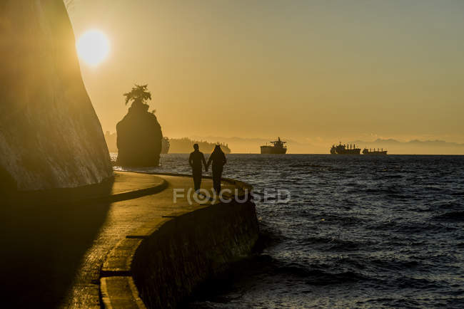 Silhuetas de casal passeando no Stanley Park Seawall ao pôr do sol, Vancouver, British Columbia, Canadá — Fotografia de Stock