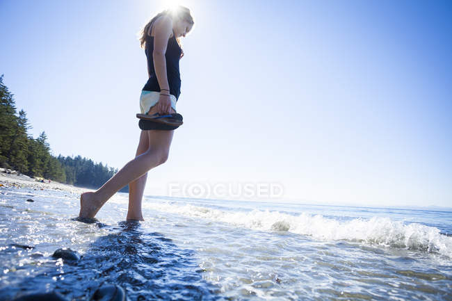 Low angle view of young woman standing barefoot in ocean at French Beach Provincial Park, Vancouver Island, Canada — Stock Photo