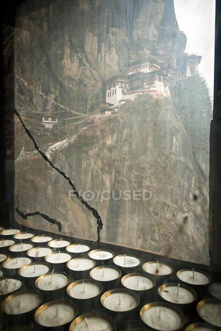 Candles and window glass with Taktsang Tigers Nest Monastery in rocks above Paro, Bhutan — Stock Photo