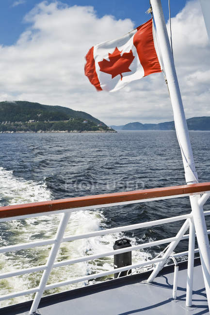 Bandera canadiense en popa de barco que monta en el río Saguenay, Pointe-Noire en Baie-Sainte-Catherine, Charlevoix, Quebec, Canadá - foto de stock