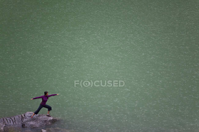 Женщина, практикующая йогу воин II позирует под дождем на озере Медисин, Национальный парк Джаспер, Альберта, Канада — стоковое фото