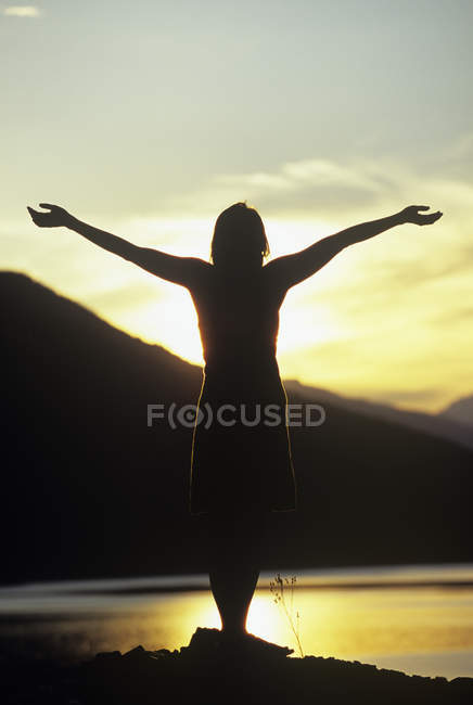 Silueta de mujer con los brazos levantados al atardecer, Columbia River, Revelstoke, Columbia Británica, Canadá . - foto de stock