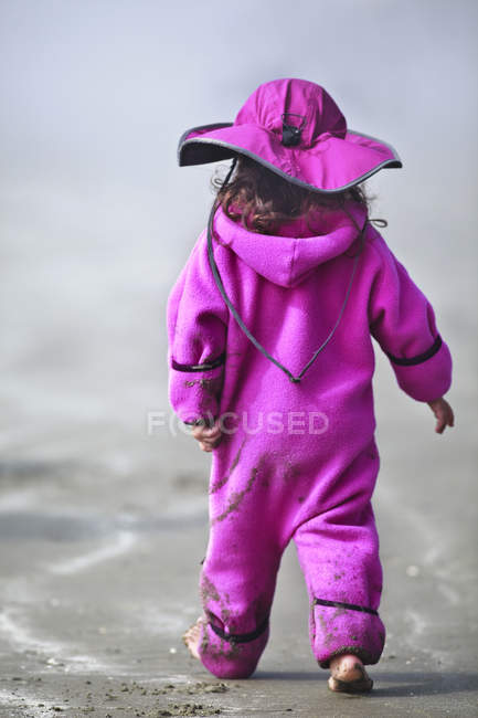 Visão traseira da menina em terno rosa andando na praia — Fotografia de Stock