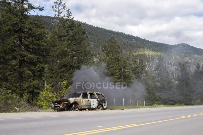 Coche en llamas en el lado de la carretera en el bosque de Canadá . - foto de stock