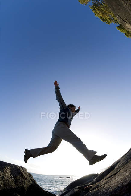 Vue en angle bas d'une randonneuse sautant sur des rochers, parc régional East Sooke, Victoria, Colombie-Britannique, Canada . — Photo de stock