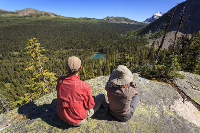 Two hikers rest at a viewpoint overlooking Egypt Lake in Banff National Park, Alberta, Canada. Model Released. — Stock Photo